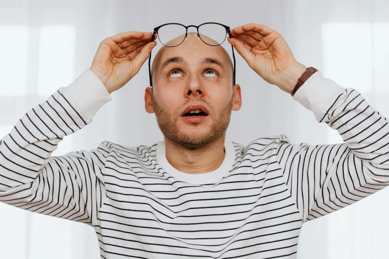 a man holding a pair of glasses over his head, inspired by Leo Leuppi, trending on pexels, hyperrealism, bald patch, charlie day, wearing stripe shirt, nootropic stimulant