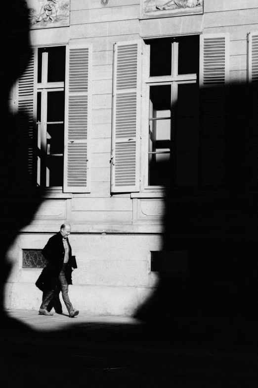 a black and white photo of a person walking in front of a building, inspired by Louis Stettner, unsplash, contre jour, paris 2010, two men, spying