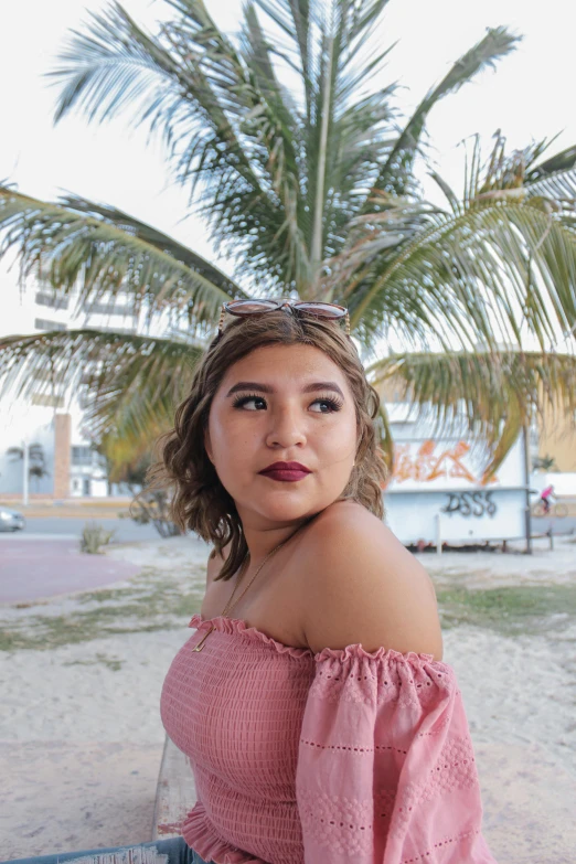 a woman sitting on a bench next to a palm tree, by reyna rochin, beutiful face, standing near the beach, thicc, journalism photo