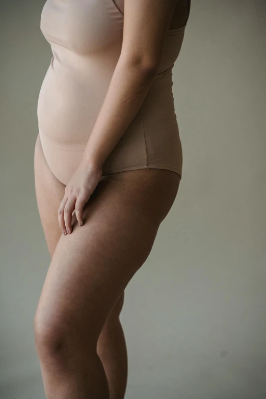 a woman in a tan underwear posing for a picture, by Matija Jama, unsplash, maternity feeling, varying thickness, thick lining, asymmetry