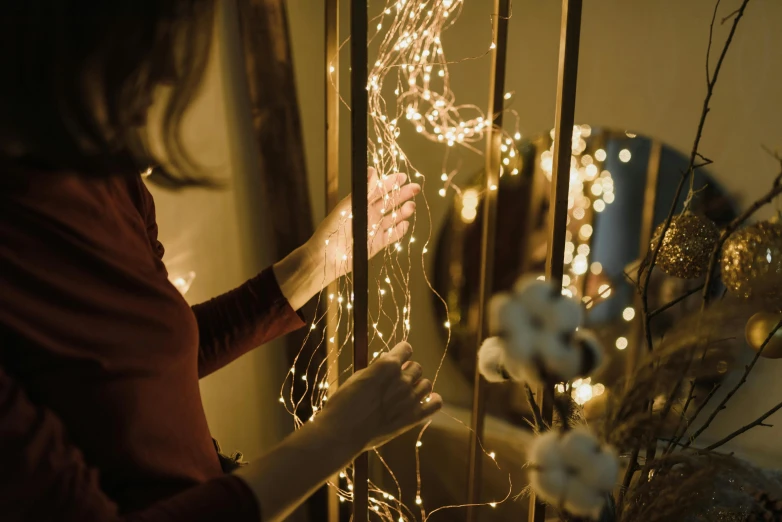 a woman that is standing in front of a window, a picture, by Julia Pishtar, pexels contest winner, light and space, fairy lights, decorations, large electrical gold sparks, beautifully soft lit