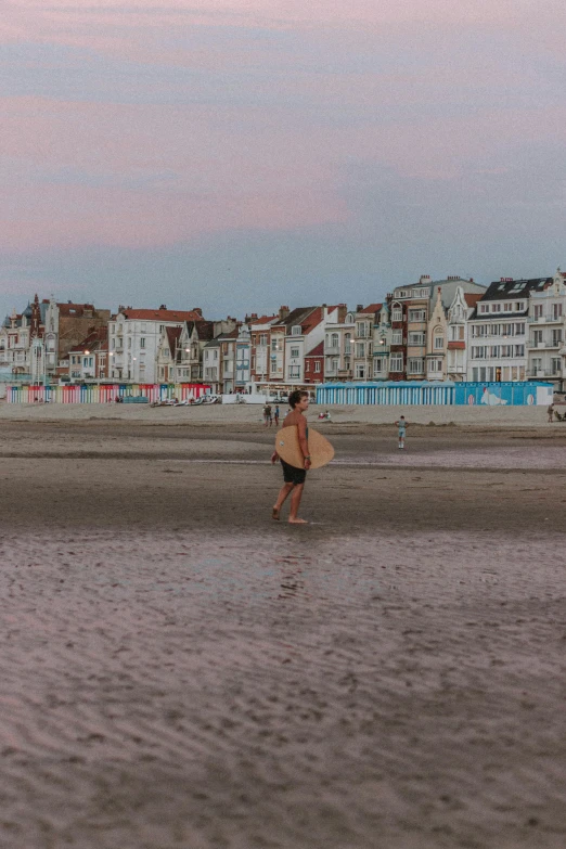 a person walking on a beach with a surfboard, a photo, by Andries Stock, unsplash contest winner, art nouveau, dunkirk, neighborhood, late evening, panoramic centered view of girl