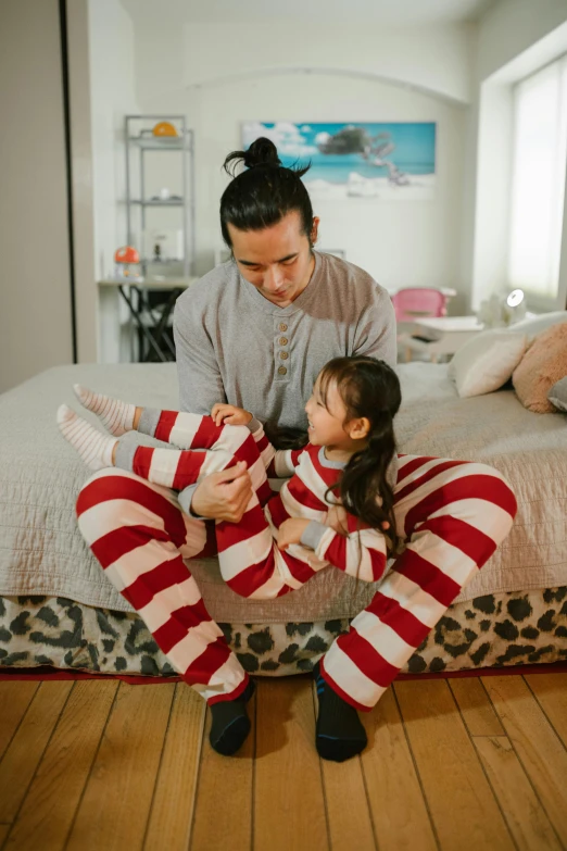 a man sitting on top of a bed next to a little girl, red and white stripes, wearing pajamas, gen z, fatherly