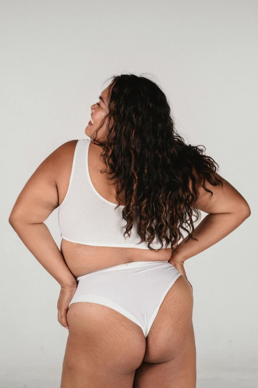 a woman in a white underwear posing for a picture, facing away from the camera, plus-sized, back view »