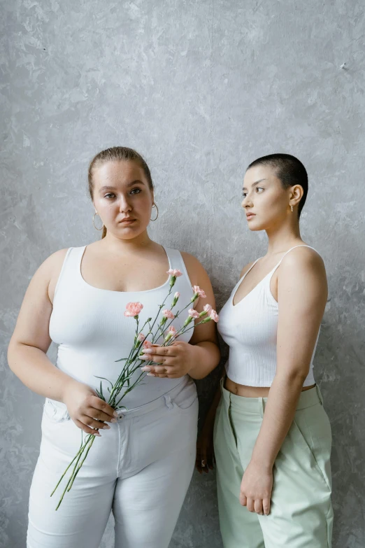 two women standing next to each other holding flowers, inspired by Vanessa Beecroft, trending on pexels, an overweight, portrait sophie mudd, promotional image, white clothing