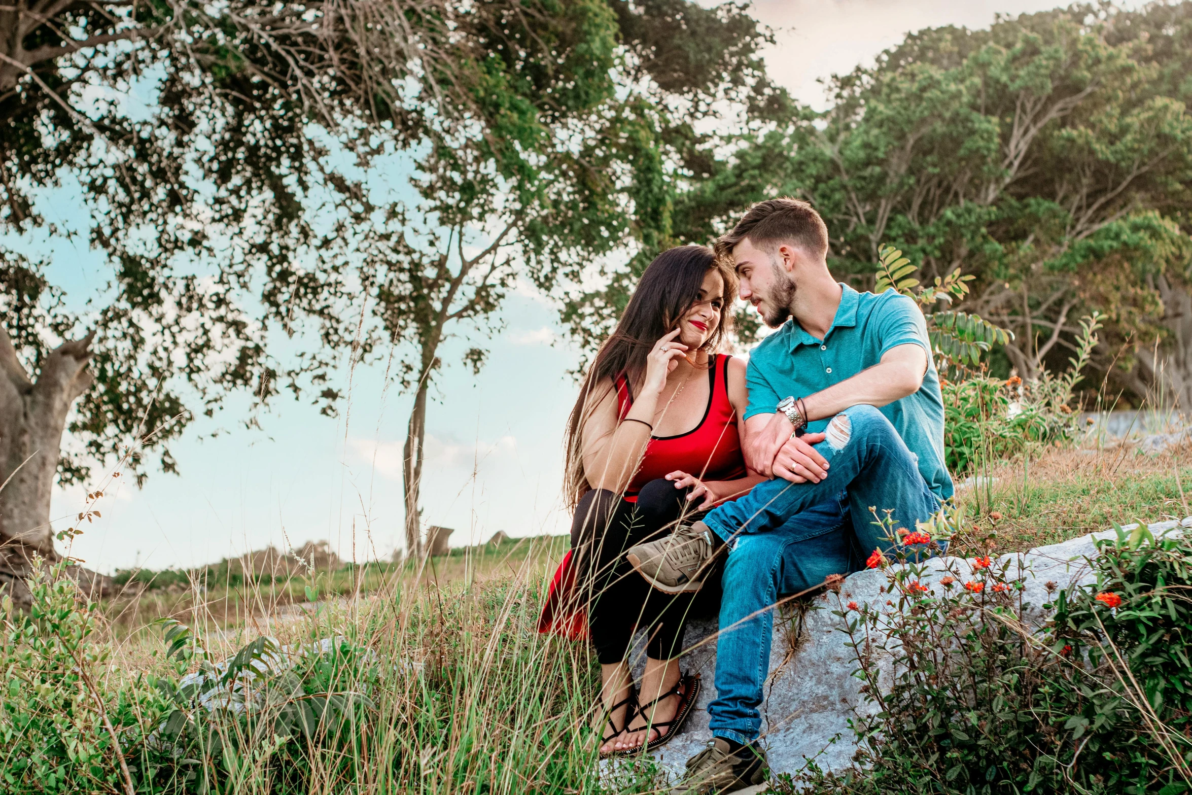 a man and woman sitting on a rock in a field, a portrait, by Milton Menasco, pexels, romanticism, avatar image, hispanic, youtube thumbnail, flirting