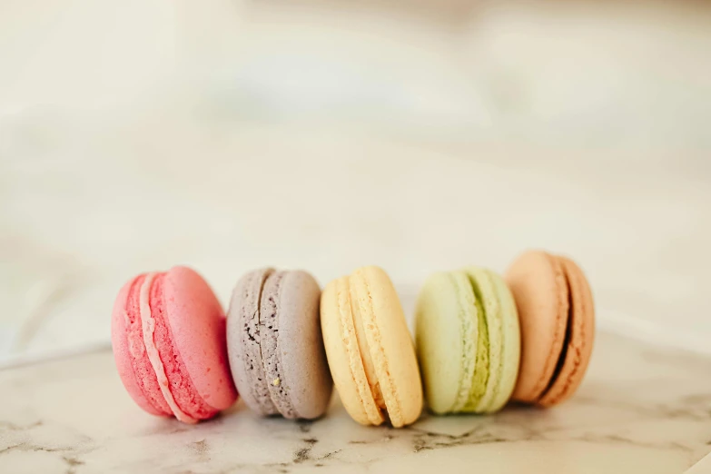 a row of macarons sitting on top of a marble counter, by Sylvia Wishart, trending on pexels, muted colours, 6 colors, press shot, chalk