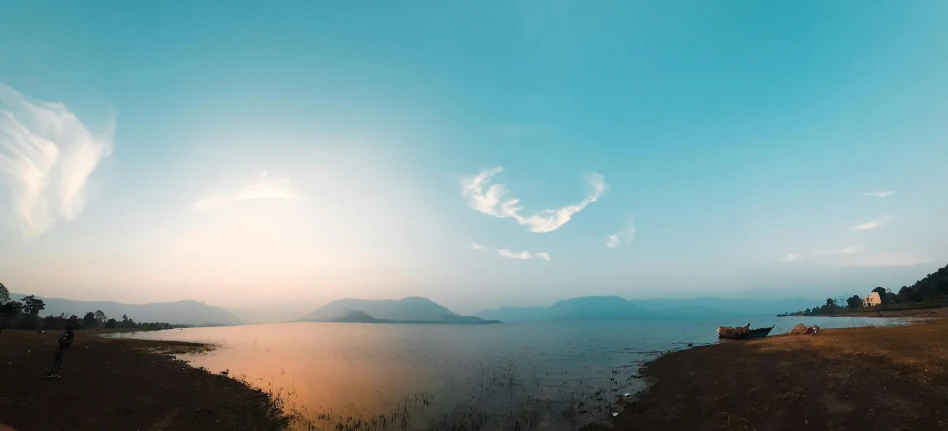 a person standing on a beach next to a body of water, pexels contest winner, romanticism, panorama view of the sky, lake kawaguchi, sunfaded, lake blue
