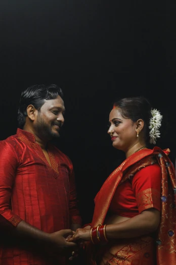 a man and woman standing next to each other, by Max Dauthendey, pexels contest winner, hurufiyya, red on black, dressed in a sari, ( ( theatrical ) ), slide show