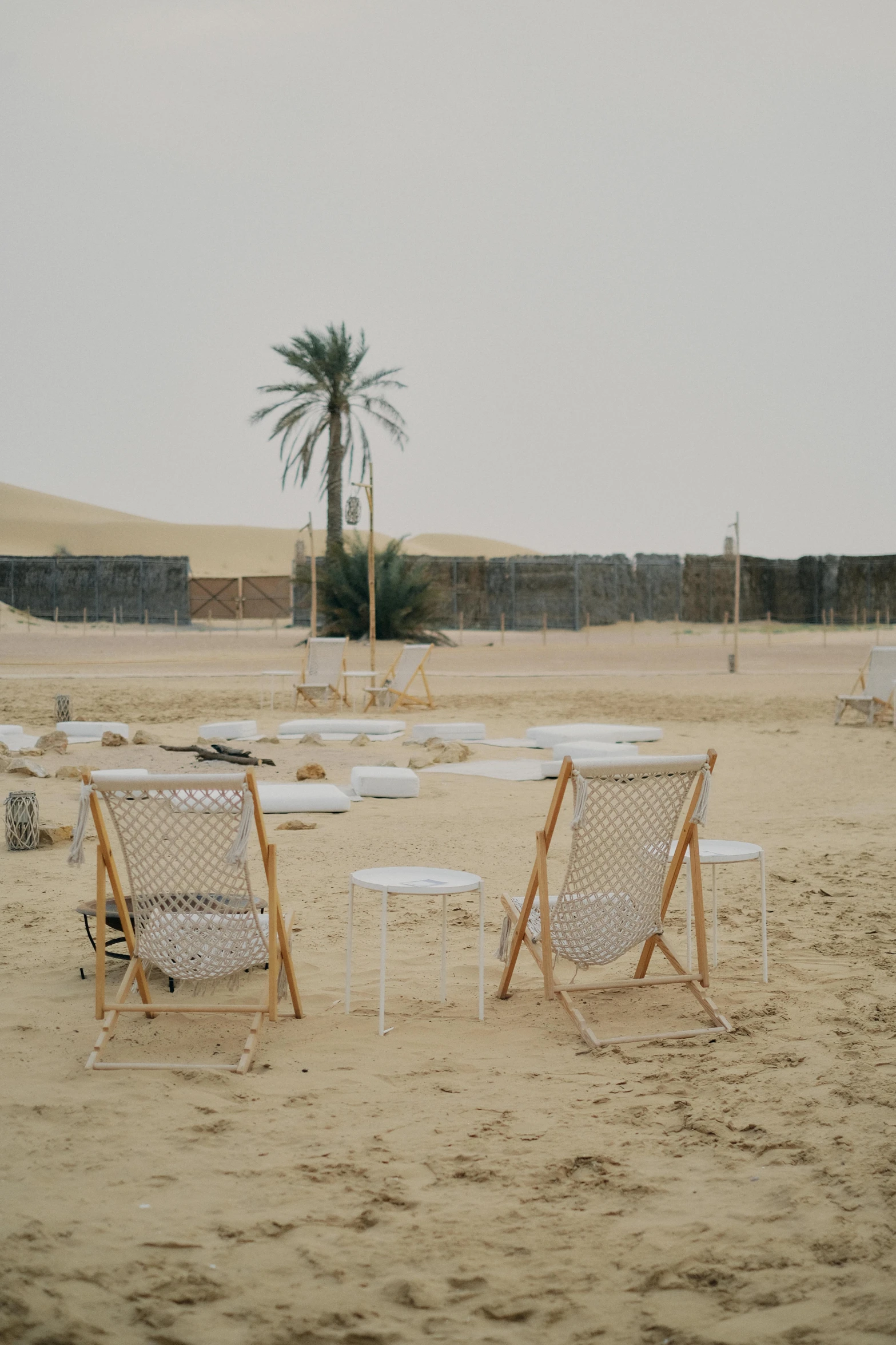 a couple of lawn chairs sitting on top of a sandy beach, land art, moroccan city, dwell, thrown tables, structures