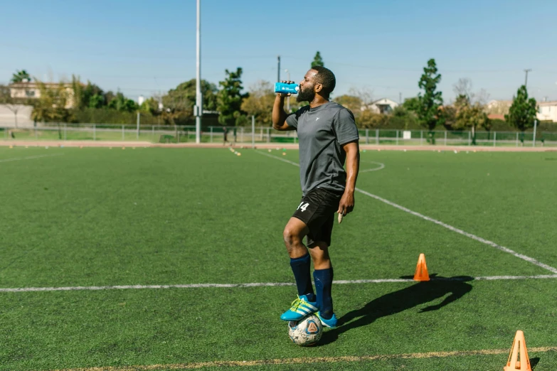 a man standing on top of a soccer field, holding a drink, working out, pitchblack skin, sydney park