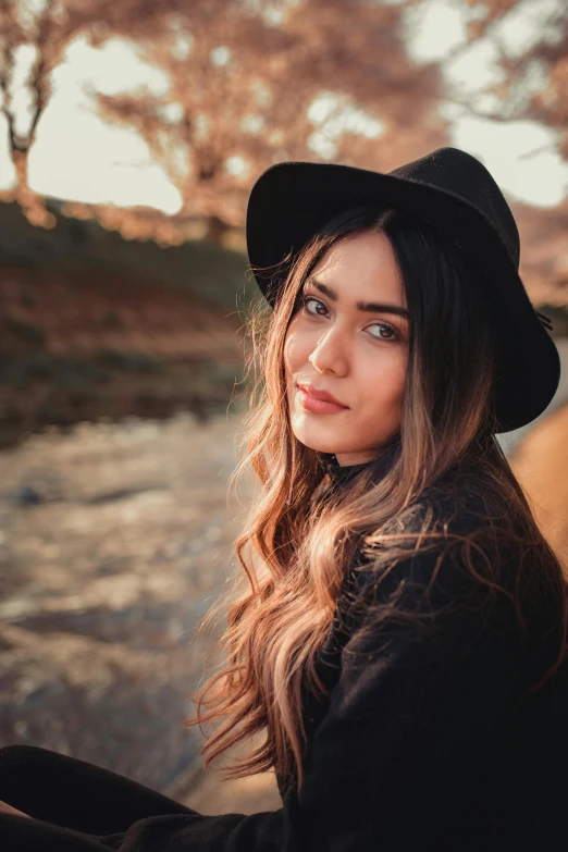 a woman sitting on a bench wearing a hat, trending on pexels, long wavy dark hair, portrait photo of a backdrop, warm glow, instagram post