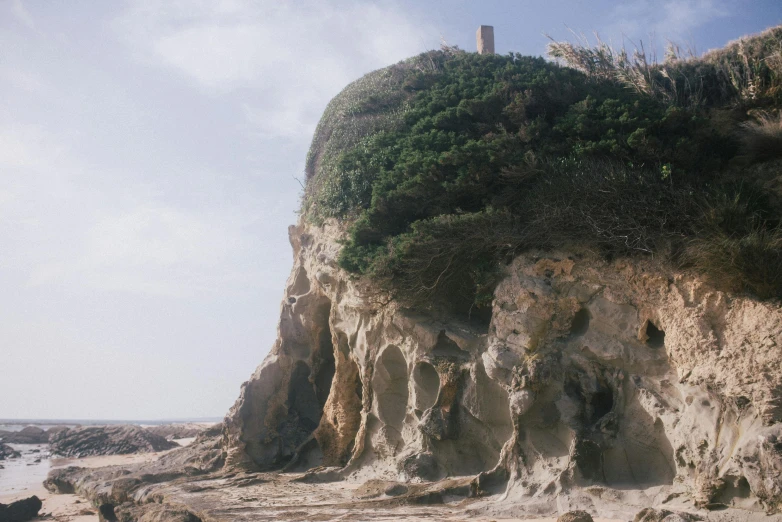 a man riding a surfboard on top of a sandy beach, an album cover, unsplash, renaissance, overgrown stone cave, house on a hill, alvaro siza, yoshifumi ushima