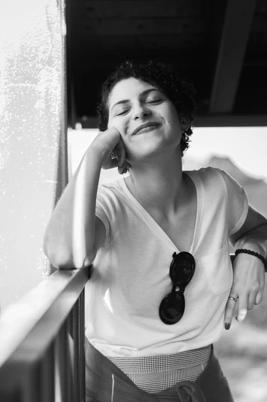 a black and white photo of a woman leaning against a wall, by Niyazi Selimoglu, dark short curly hair smiling, on a boat, on a bright day, raphael personnaz