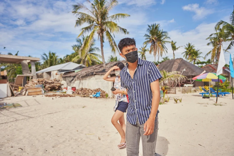 a man holding a child on a beach, by Julia Pishtar, pexels contest winner, shin hanga, wearing bandit mask, village in the background, rodrigo duterte, in front of the house