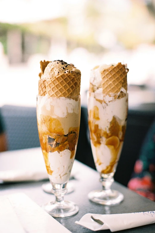 two ice cream sundaes sitting on top of a table, unsplash, honeycomb, tall, tan, brazilian