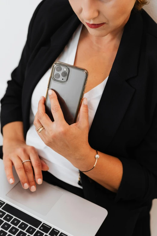 a woman holding a cell phone next to a laptop, metallic bronze skin, detailed product image, curated collections, holding arms on holsters