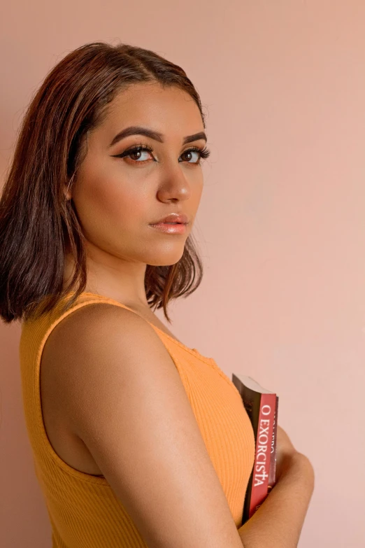 a woman in a yellow dress holding a book, an album cover, inspired by Glòria Muñoz, trending on pexels, thick bushy straight eyebrows, light red and deep orange mood, headshot photoshoot, violet myers