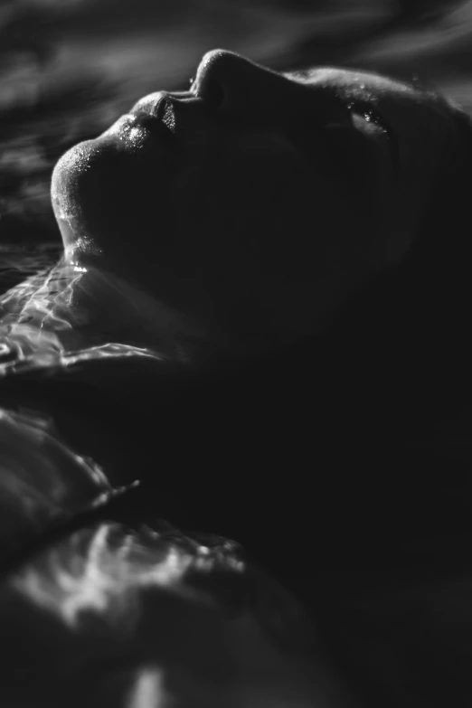 a black and white photo of a woman in the water, a black and white photo, by Adam Marczyński, unsplash, conceptual art, lying in bed, light glare, profile image, summer night