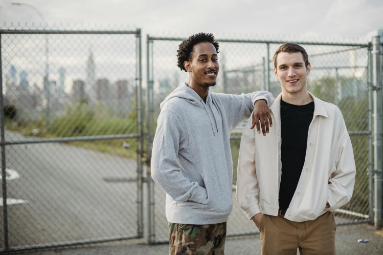 two men standing next to each other in front of a fence, a portrait, unsplash, brooklyn background, thin young male, background image, various posed