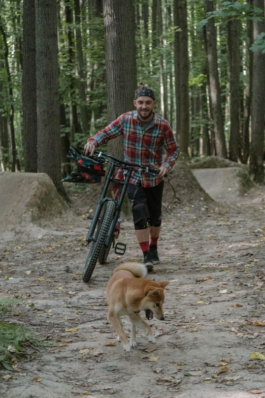 a man riding a bike down a dirt road next to a dog, woods, posing for camera, profile image