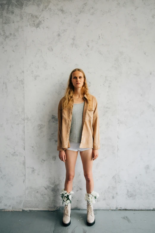 a woman standing in front of a wall, unsplash, wear's beige shirt, dressed in short leather jacket, wearing shorts and t shirt, britt marling style 3/4