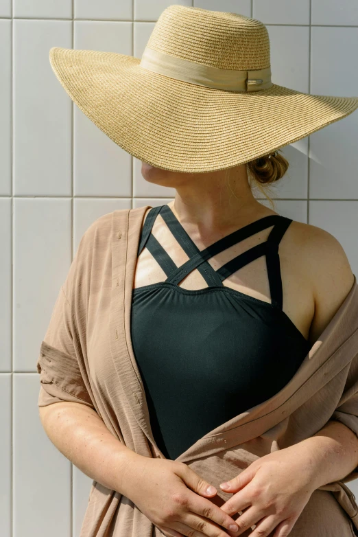 a woman standing in front of a wall wearing a hat, inspired by Caro Niederer, unsplash, renaissance, black swimsuit, in a sun lounger, close - up photograph, wearing cross on robe