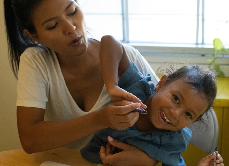 a woman sitting at a table with a child, pexels contest winner, holding a magic needle, manuka, schools, nursing