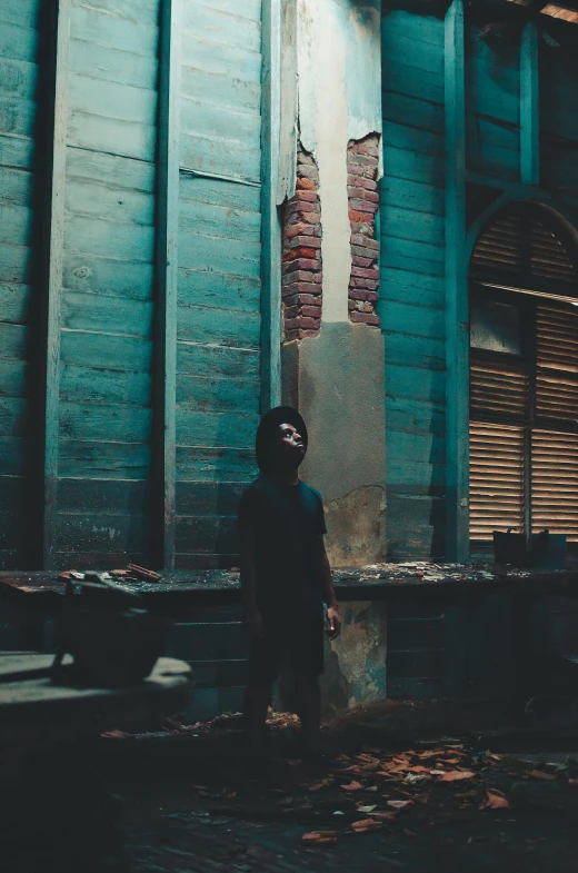 a person in a hoodie standing in front of a building, inspired by Elsa Bleda, pexels contest winner, conceptual art, damaged structures, man in dark blue full body suit, ( ( theatrical ) ), vintage color