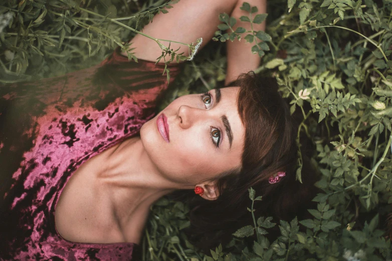 a woman laying on top of a lush green field, inspired by Elsa Bleda, pexels contest winner, magic realism, looking up at camera, natalia dyer, in pink forest, high angle closeup portrait