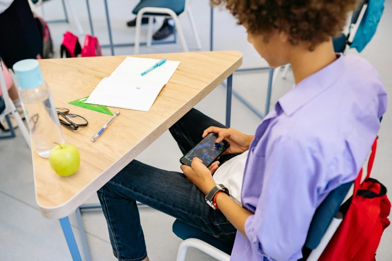 a person sitting at a table with a cell phone, school, holding an apple, playing games, standing on a desk