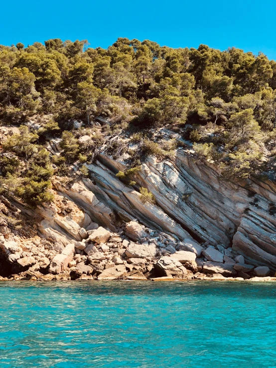 a man riding a surfboard on top of a body of water, calanque, rich deep colours, shiny layered geological strata, pine forests