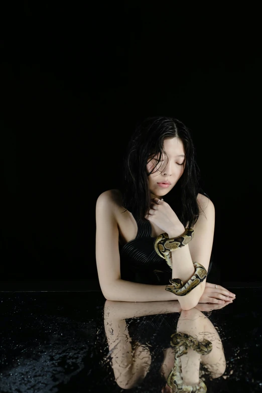 a woman sitting in the water with a snake on her arm, an album cover, inspired by Fuyuko Matsui, unsplash, dark backdrop, portrait of mayuri shiina, sitting with wrists together, 2010s