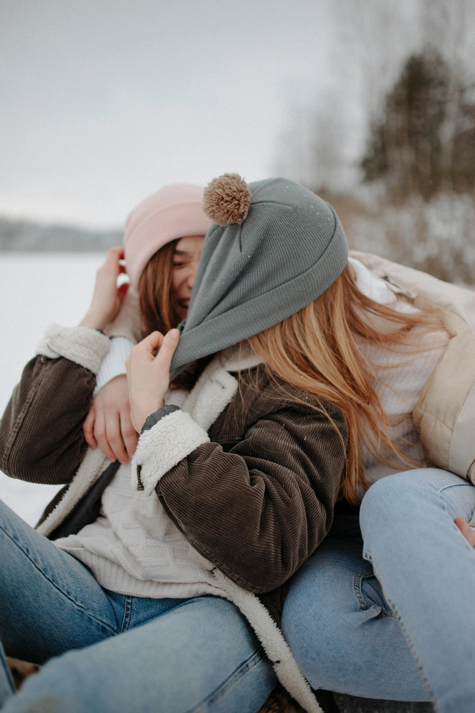 two women sitting next to each other in the snow, trending on pexels, beanie, hugging each other, soft cool colors, digital image