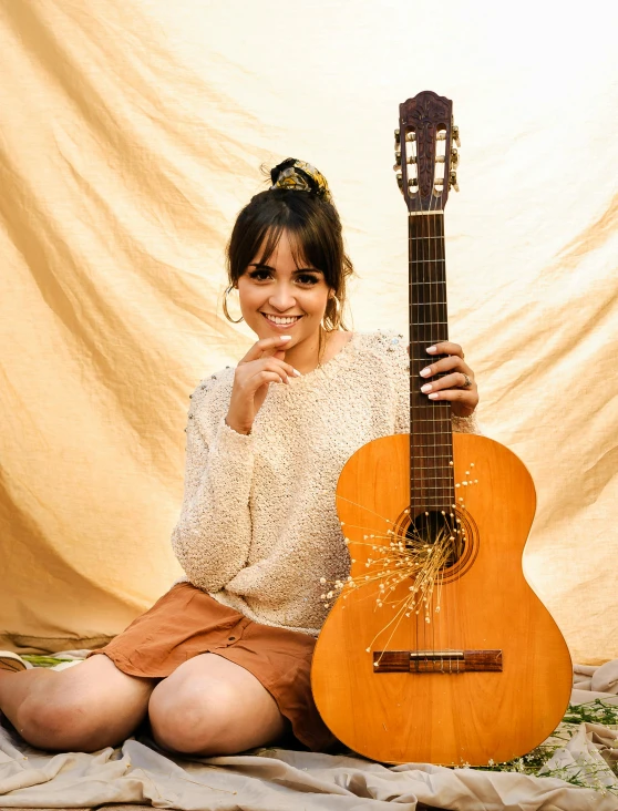 a woman sitting on the ground with a guitar, an album cover, inspired by Glòria Muñoz, pexels contest winner, dau-al-set, relaxed. gold background, boke, isabela moner, joyful smirk