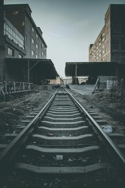 a black and white photo of a train track, inspired by Elsa Bleda, outdoors ruined cityscape, abandoned buildings, unsplash photography, abandoned warehouse