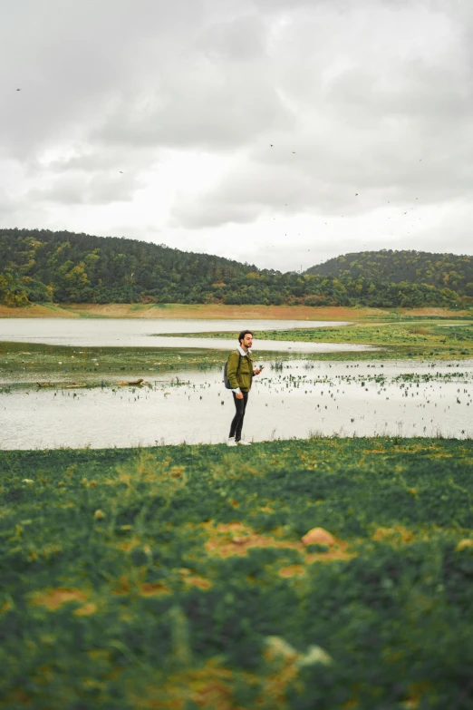 a man standing on top of a lush green field, in the middle of a lake, arrendajo in avila pinewood, rain lit, lookbook