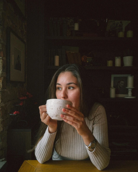 a woman sitting at a table drinking out of a cup, pexels contest winner, happening, wearing a white sweater, pokimane, profile image, actual photo