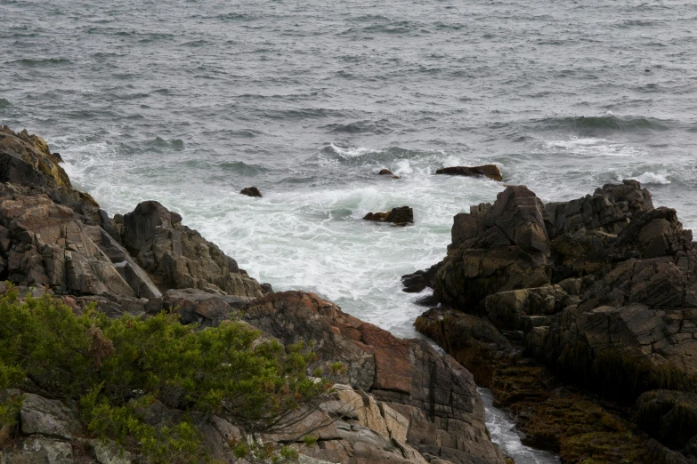 a man standing on top of a rocky cliff next to the ocean, a picture, inspired by William Trost Richards, unsplash, overcast day, currents, granite, seen from a distance