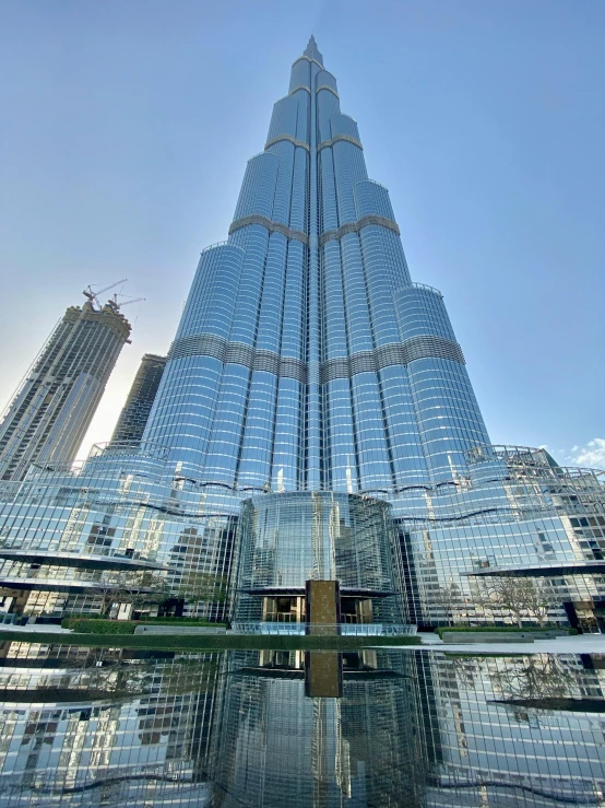 a very tall building in the middle of a city, dubai, with shiny glass buildings, fountain in the middle, thumbnail