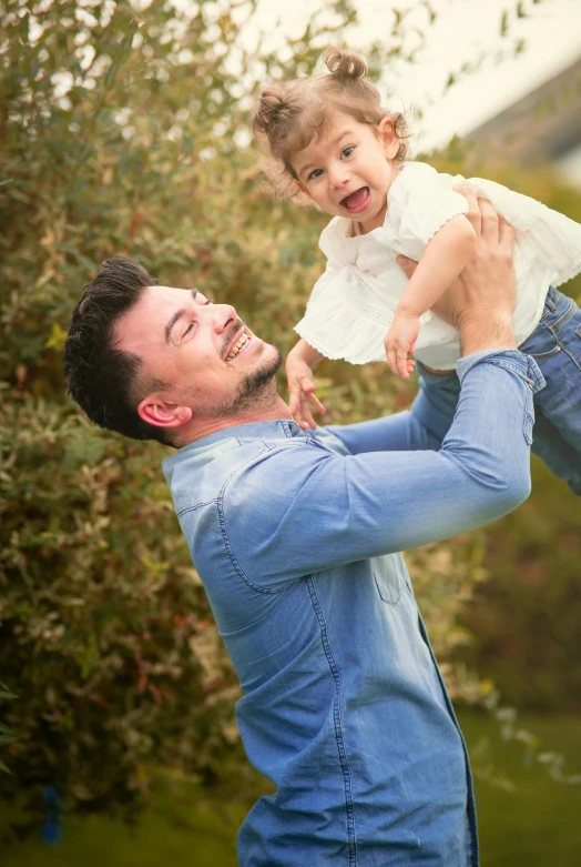 a man holding a little girl up in the air, pexels contest winner, david gandy, white shirt and blue jeans, square, paul barson