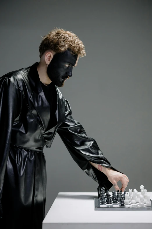 a man dressed in black playing a game of chess, an album cover, inspired by Nicola Samori, bauhaus, bodypaint, black reflect robe, with black, neoprene