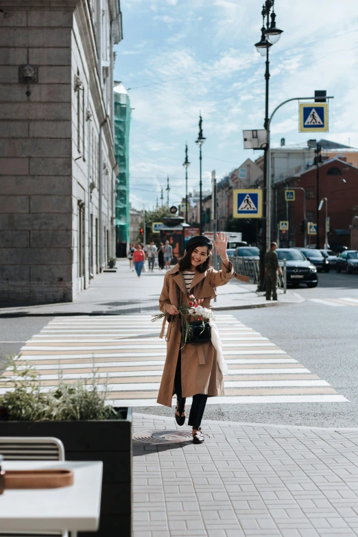 a woman walking down a sidewalk in a city, by Julia Pishtar, pexels contest winner, excited russians, trench coat, intersection, with flowers