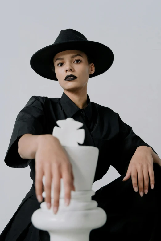 a woman sitting on top of a white chess board, an album cover, by Cosmo Alexander, unsplash, wearing black witch hat, nonbinary model, suit vest and top hat and gloves, mixed-race woman