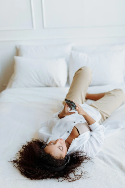 a woman laying on top of a white bed, trending on pexels, happening, looking at his phone, white dress shirt, woman is curved, gif