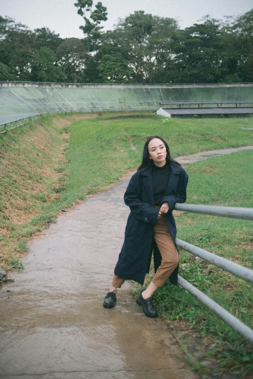 a woman leaning against a fence in the rain, an album cover, inspired by Natasha Tan, unsplash, realism, he is wearing a black trenchcoat, standing in a pond, set on singaporean aesthetic, wearing track and field suit