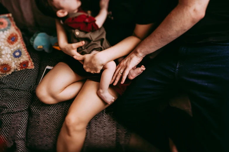 a man holding a baby while sitting on a couch, by Sam Black, pexels contest winner, incoherents, thighs close up, laying on her back, husband wife and son, coloured photo