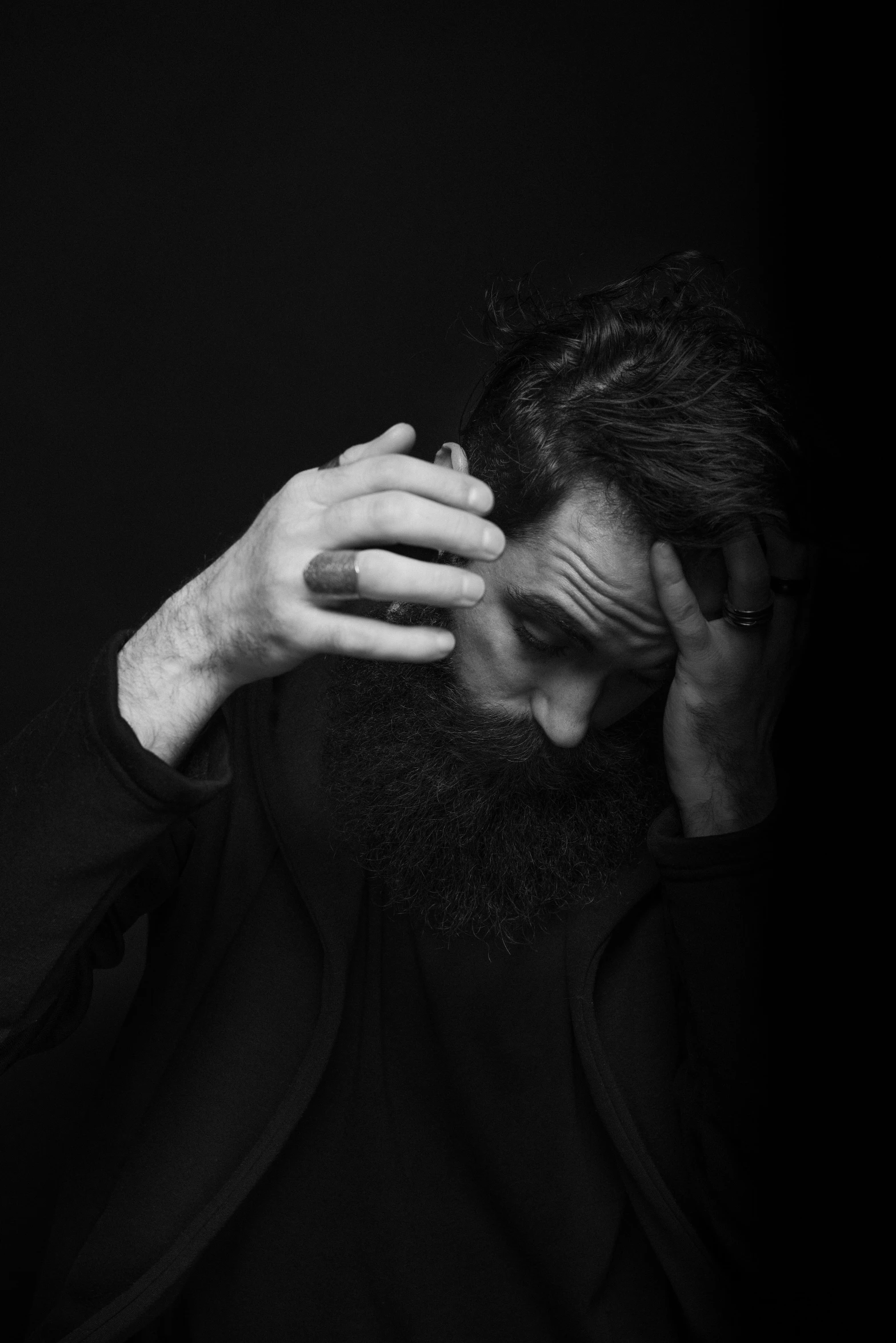 a black and white photo of a man with a beard, inspired by Lee Jeffries, unsplash, surrealism, facepalm, jim carrey, holy man looking at ground, alternate album cover