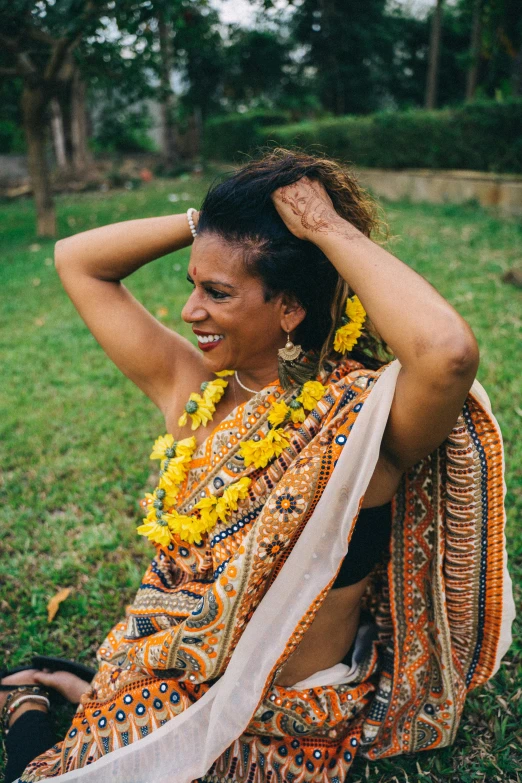 a woman sitting on top of a lush green field, intricate african jewellery, with yellow flowers around it, sarong, smiling and dancing