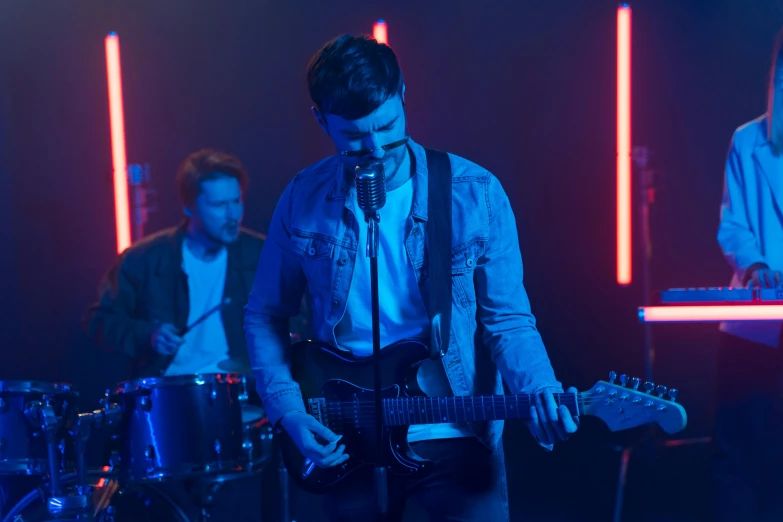 a group of men standing next to each other on a stage, an album cover, pexels, blue and red lights, man playing guitar, tv commercial, ryan dening